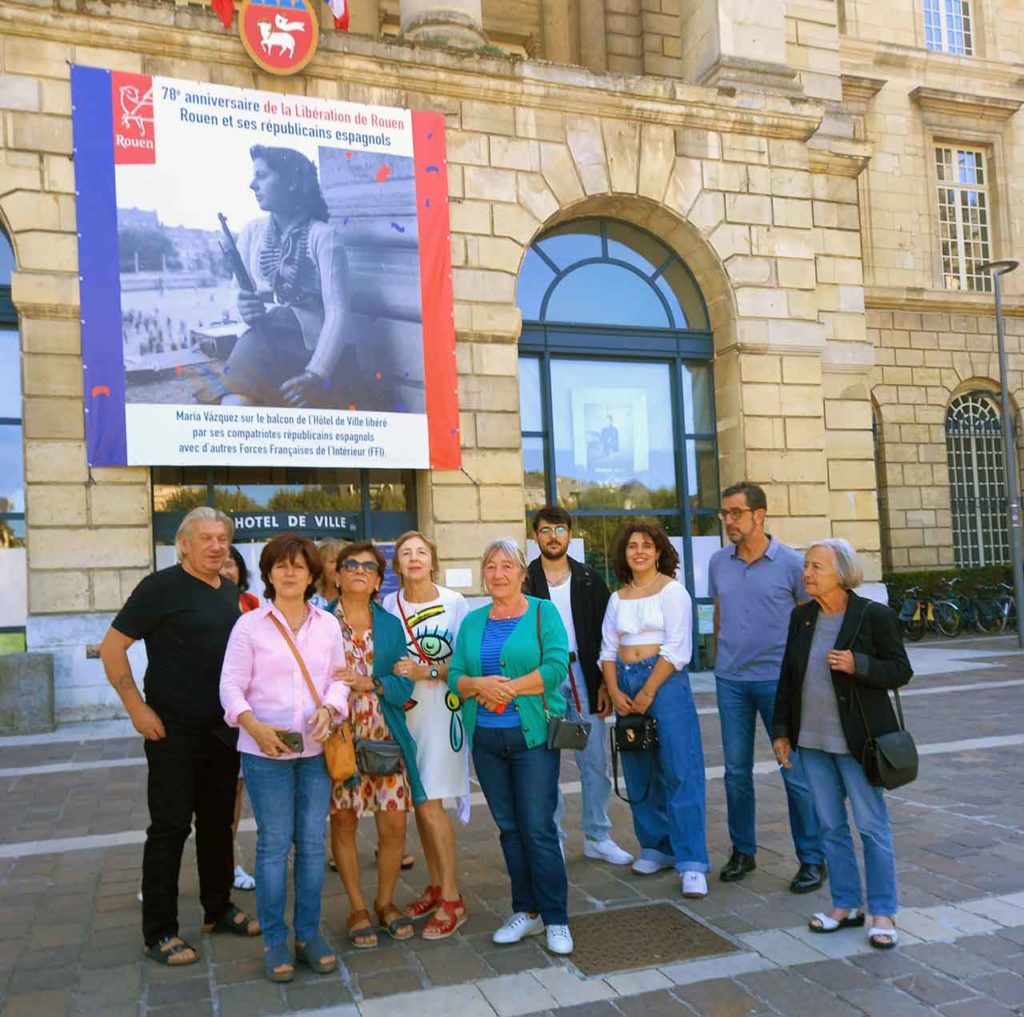 Asistentes al acto frente al cartel colocado en la fachada del Ayuntamiento de Rouen.